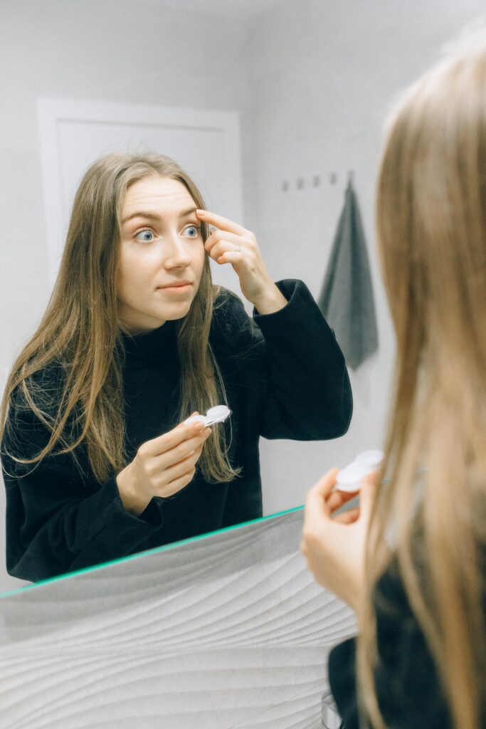 Woman lookin into mirror as she inserts contact lenses into her eye
