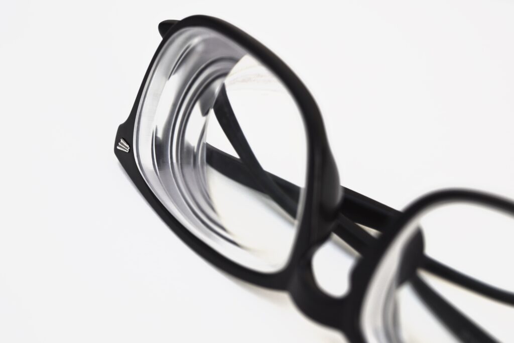 Pair of black eyeglasses laying upside down against a white background. The lenses are thick and have many reflections.